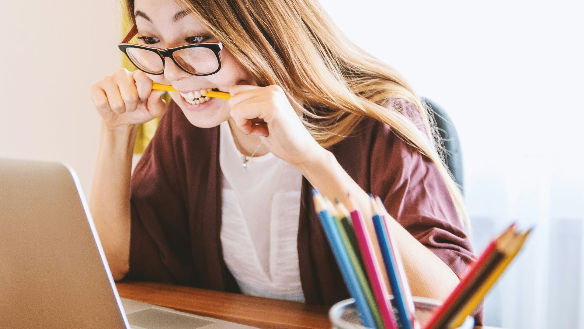 woman biting pencil while sitting on chair in front of computer during daytime