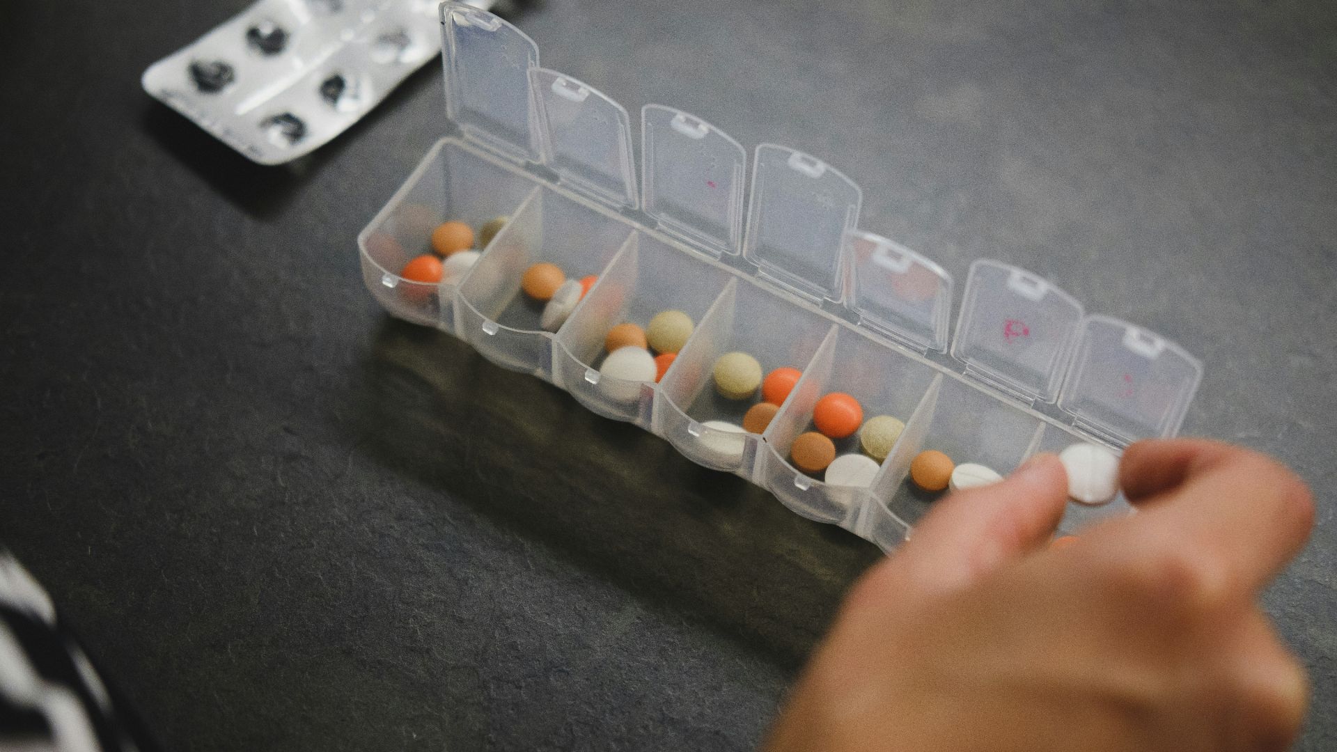 person about to pick medicine from medicine organizer