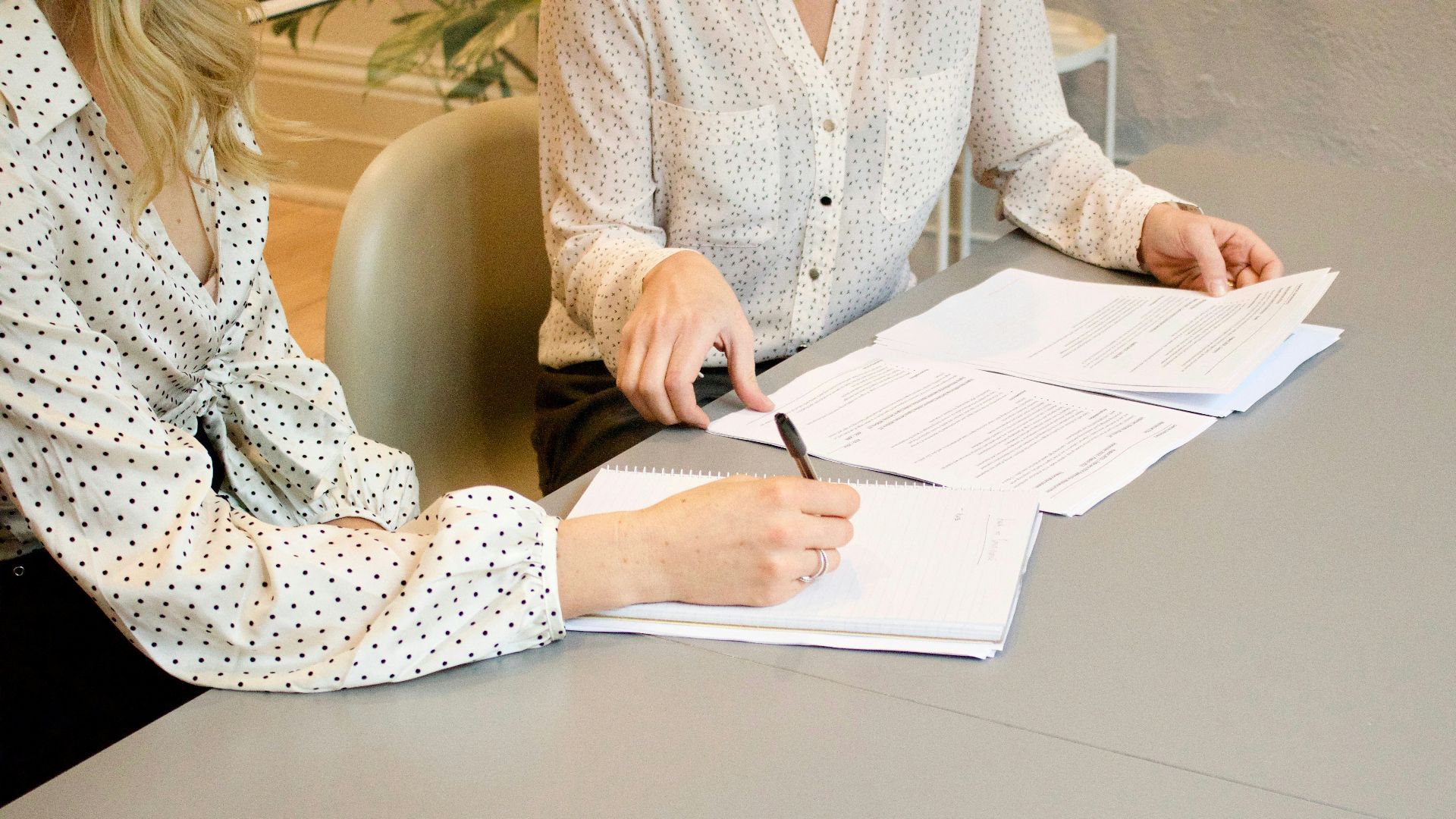 woman signing on white printer paper beside woman about to touch the documents