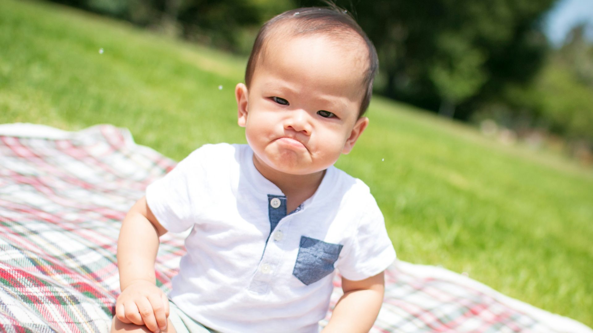 selective focus photography of grumpy face toddler sitting on plaid pad taken during daytime