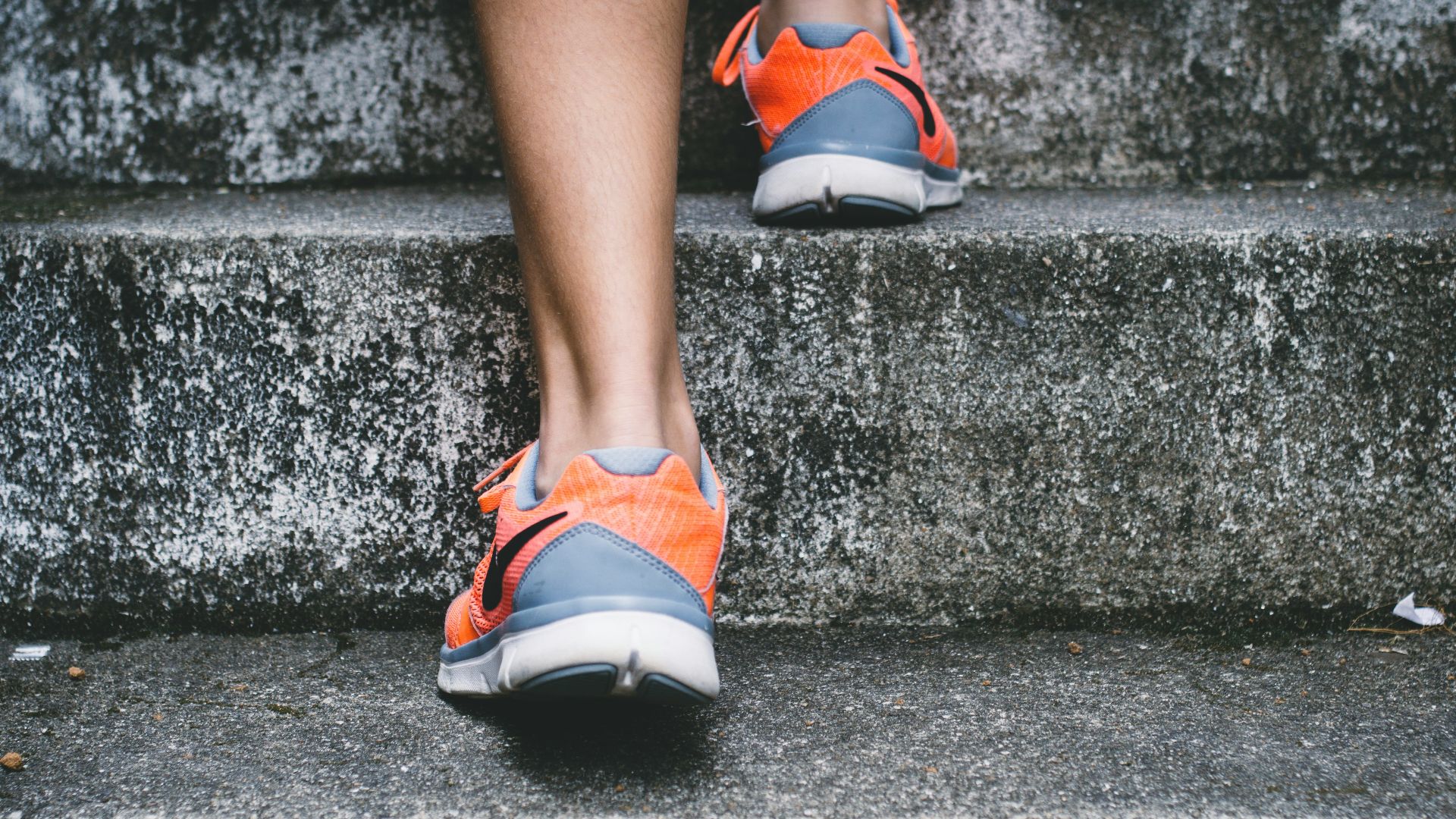 person wearing orange and gray Nike shoes walking on gray concrete stairs