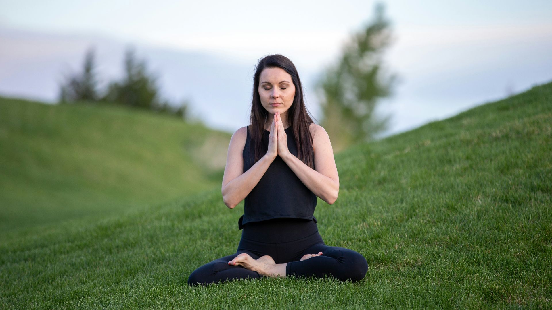 woman in black tank top and black pants sitting on green grass field during daytime