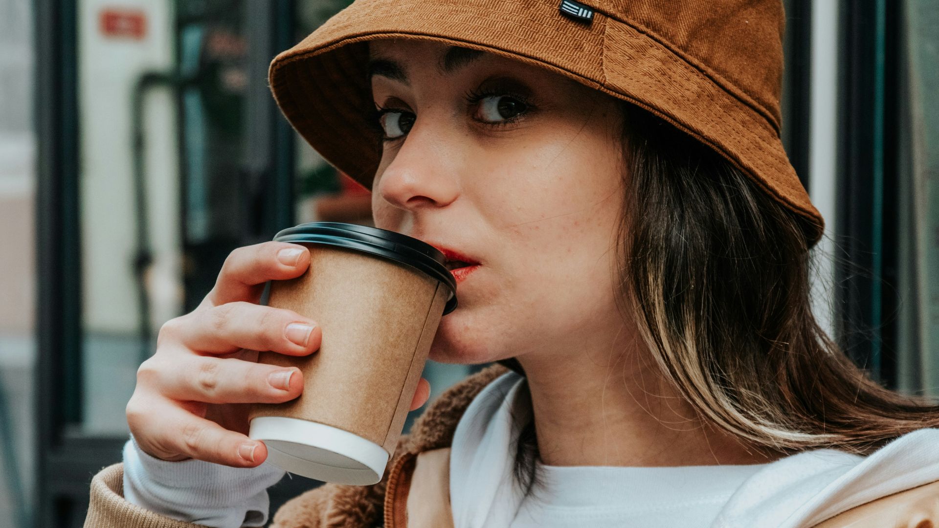 woman in brown coat holding white ceramic mug