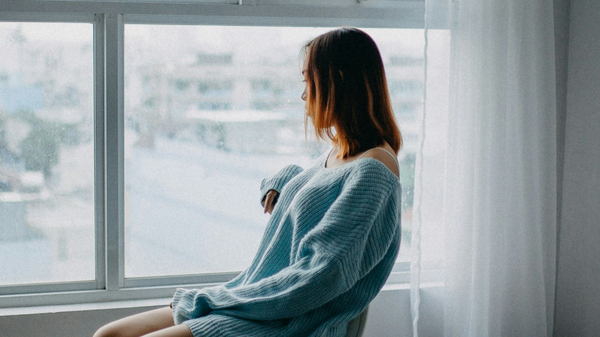 woman sitting on brown chair beside glass window