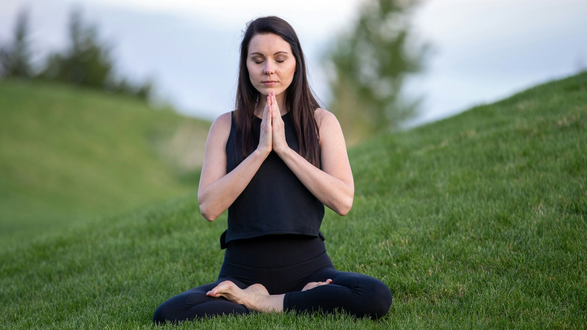 woman in black tank top and black pants sitting on green grass field during daytime