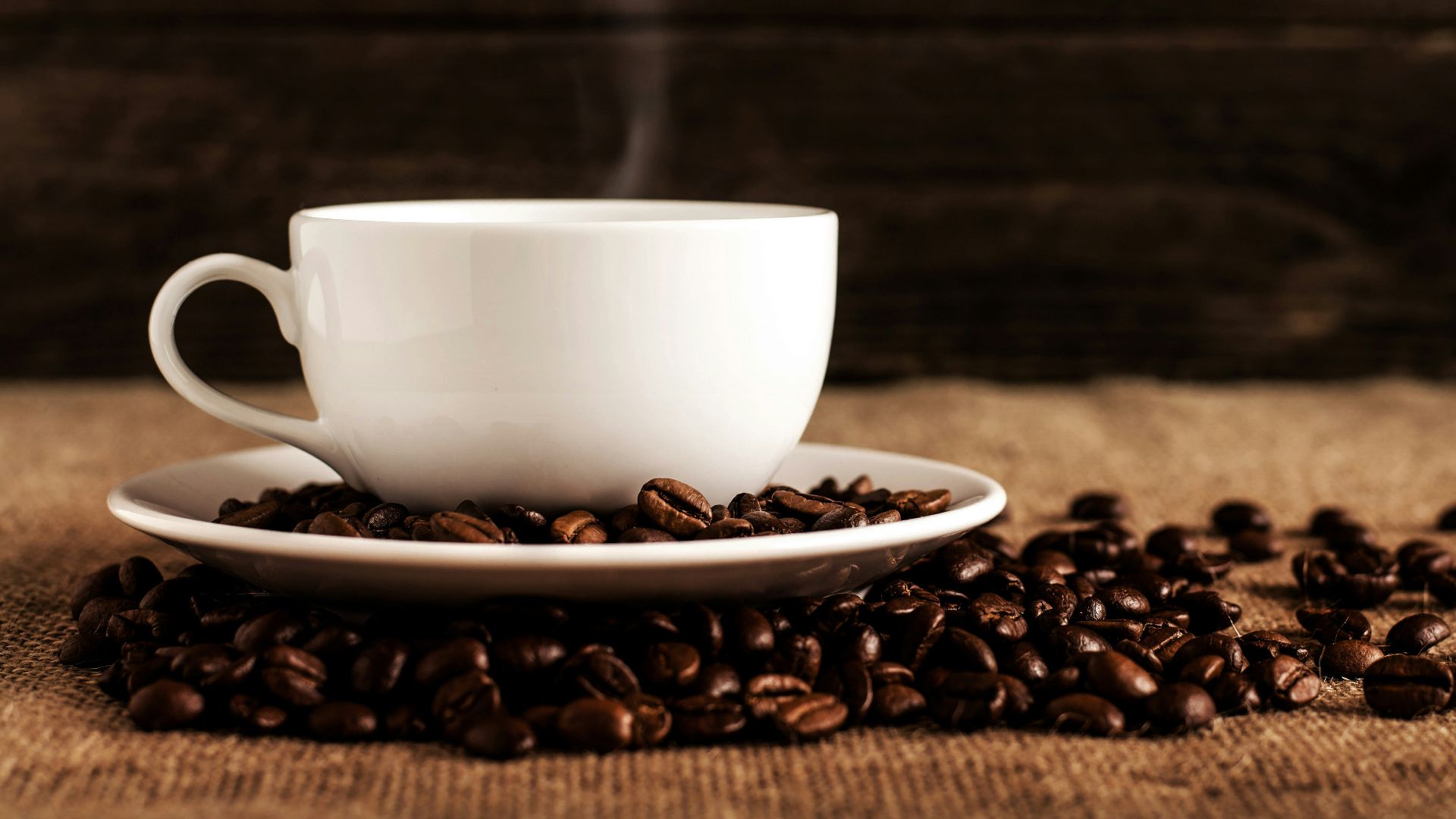 white ceramic mug and saucer with coffee beans on brown textile