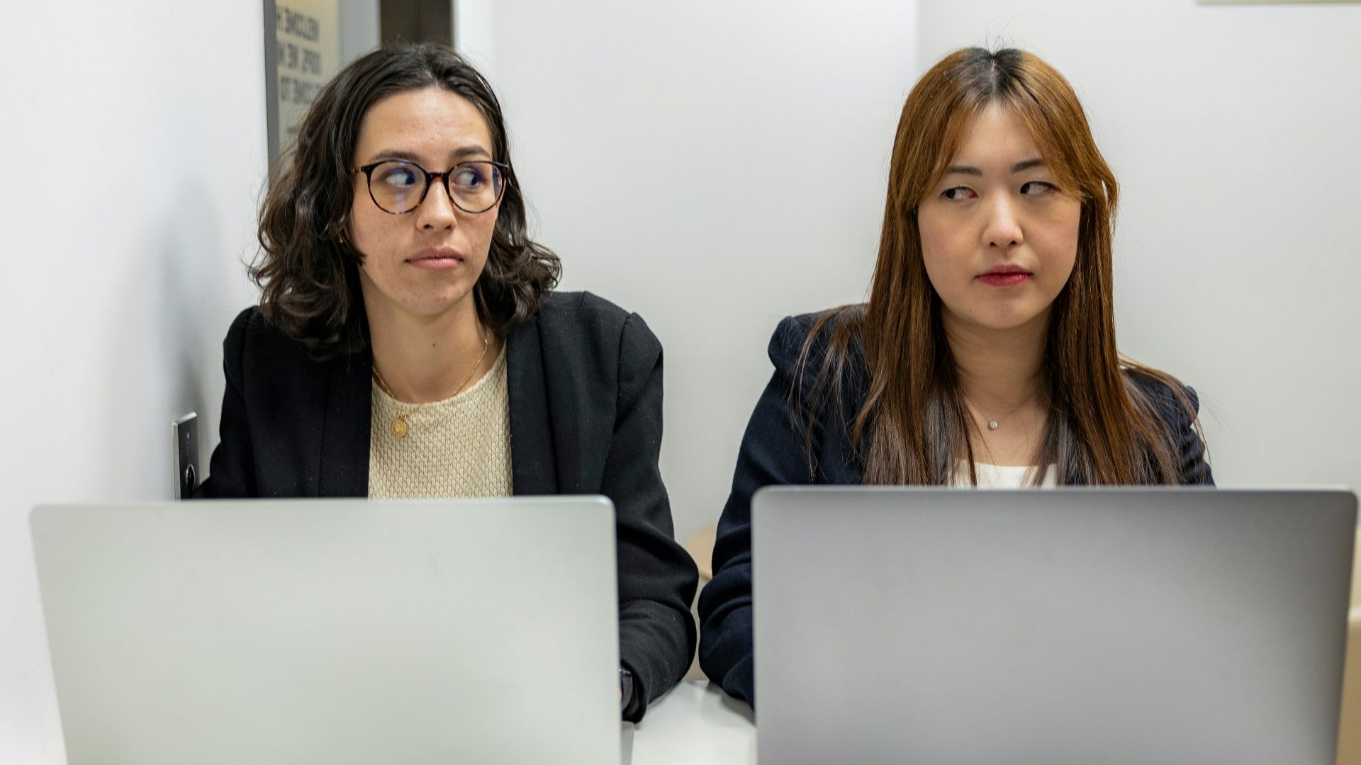two women sitting at a table with laptops