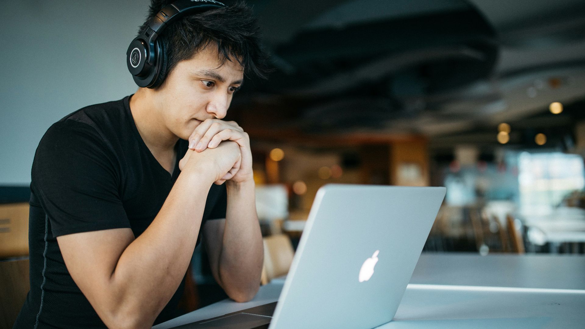 man wearing headphones while sitting on chair in front of MacBook