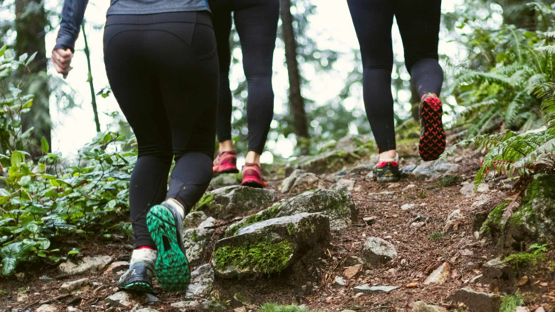 person in black leggings and green sneakers standing on brown rock