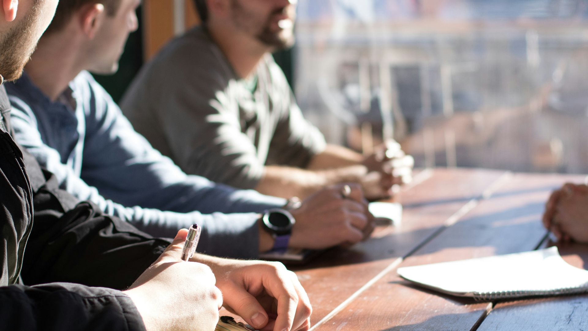 people sitting on chair in front of table while holding pens during daytime