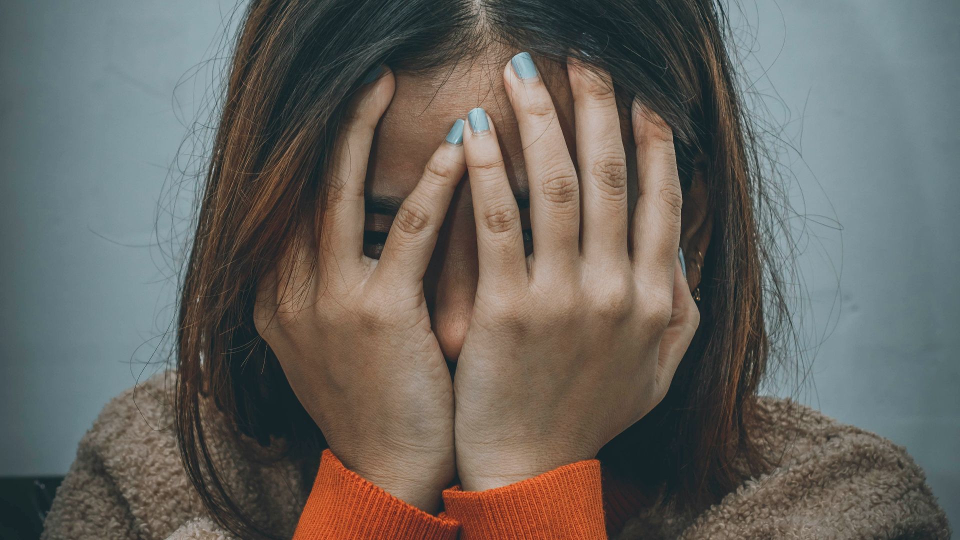 woman in brown sweater covering her face with her hand