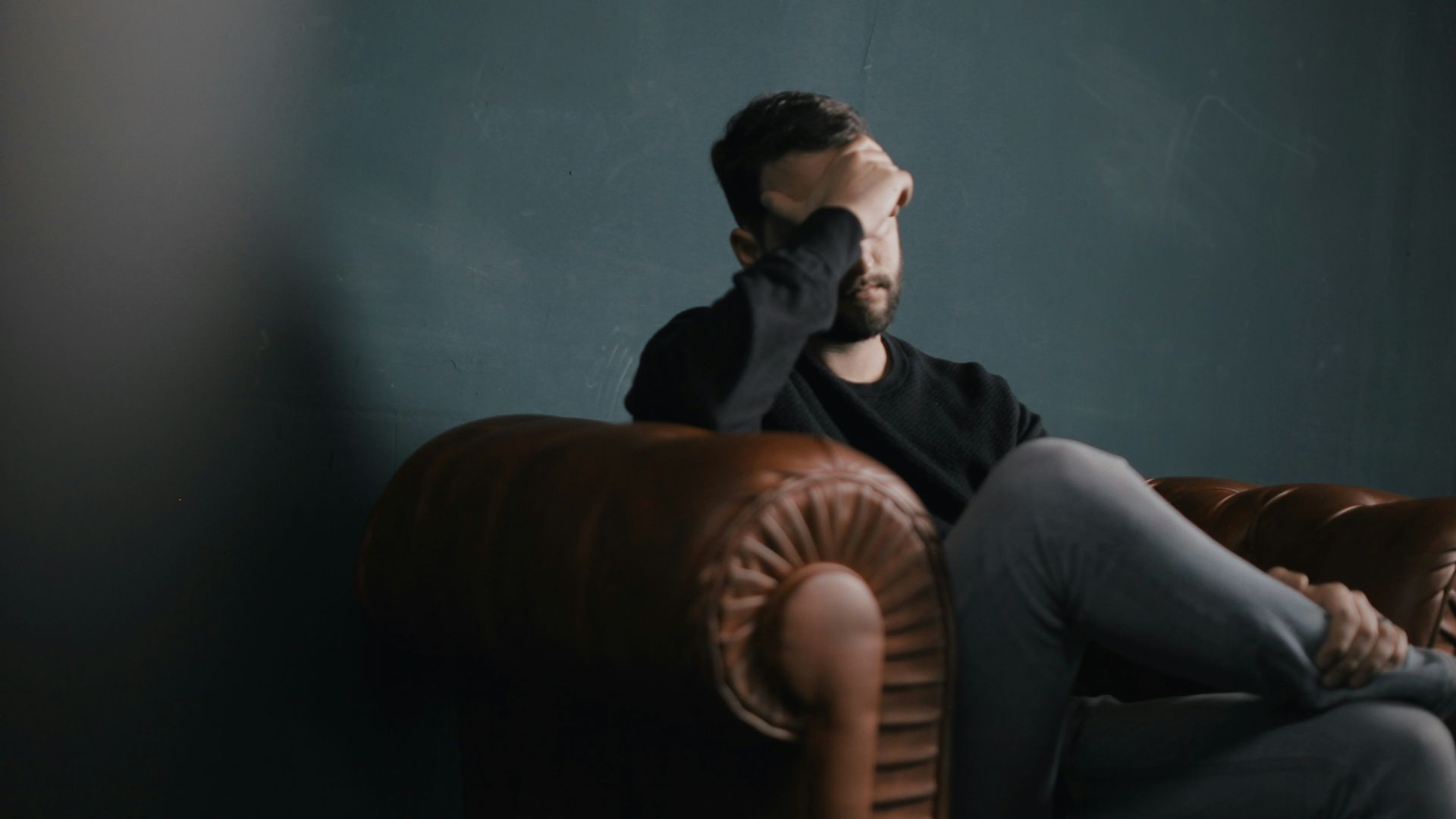 a man holds his head while sitting on a sofa