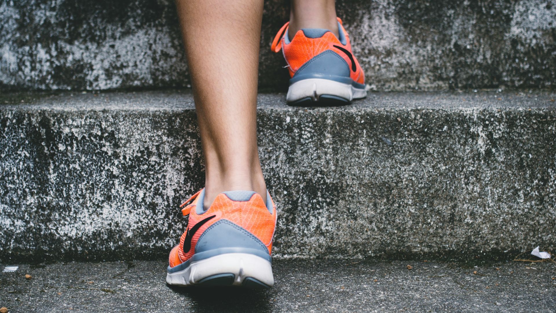 person wearing orange and gray Nike shoes walking on gray concrete stairs