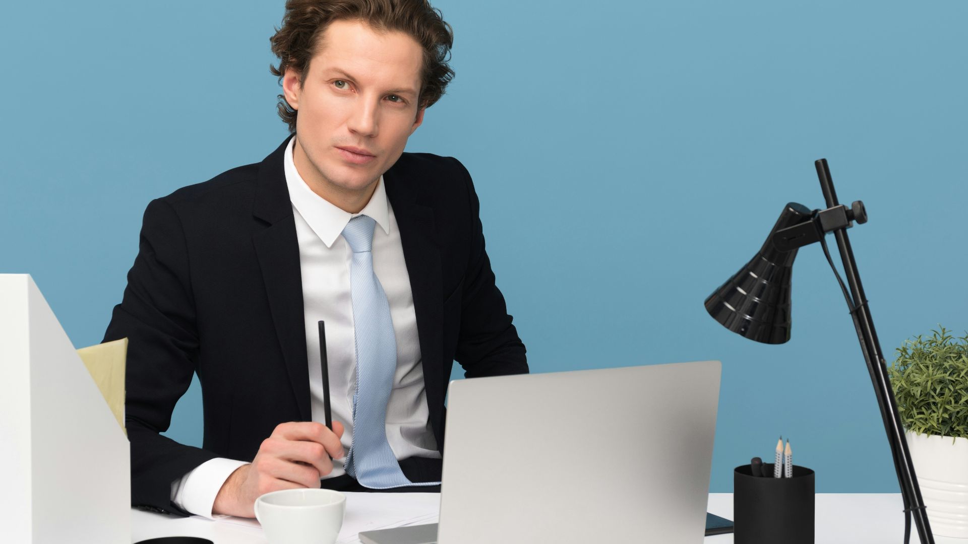 man sitting on chair beside laptop computer and teacup