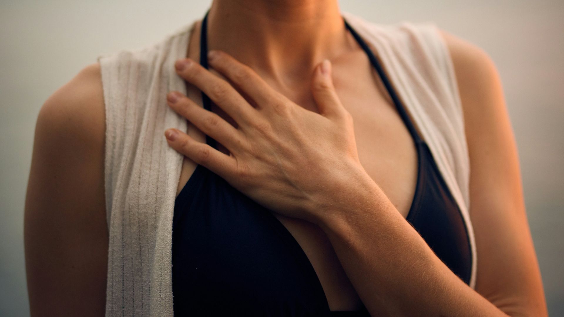 woman in white vest and black bikini with hand on chest