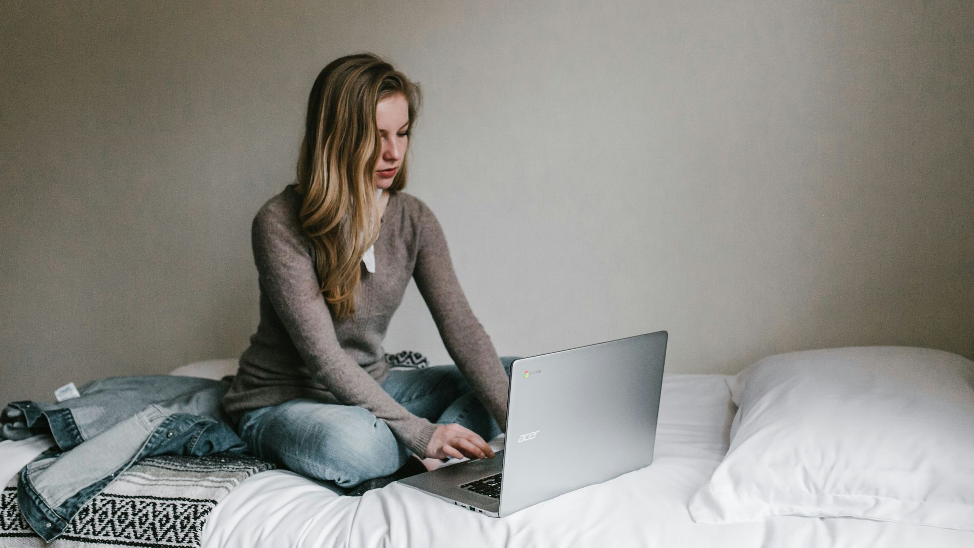 woman typing on MacBook Pro while sitting on bed in room