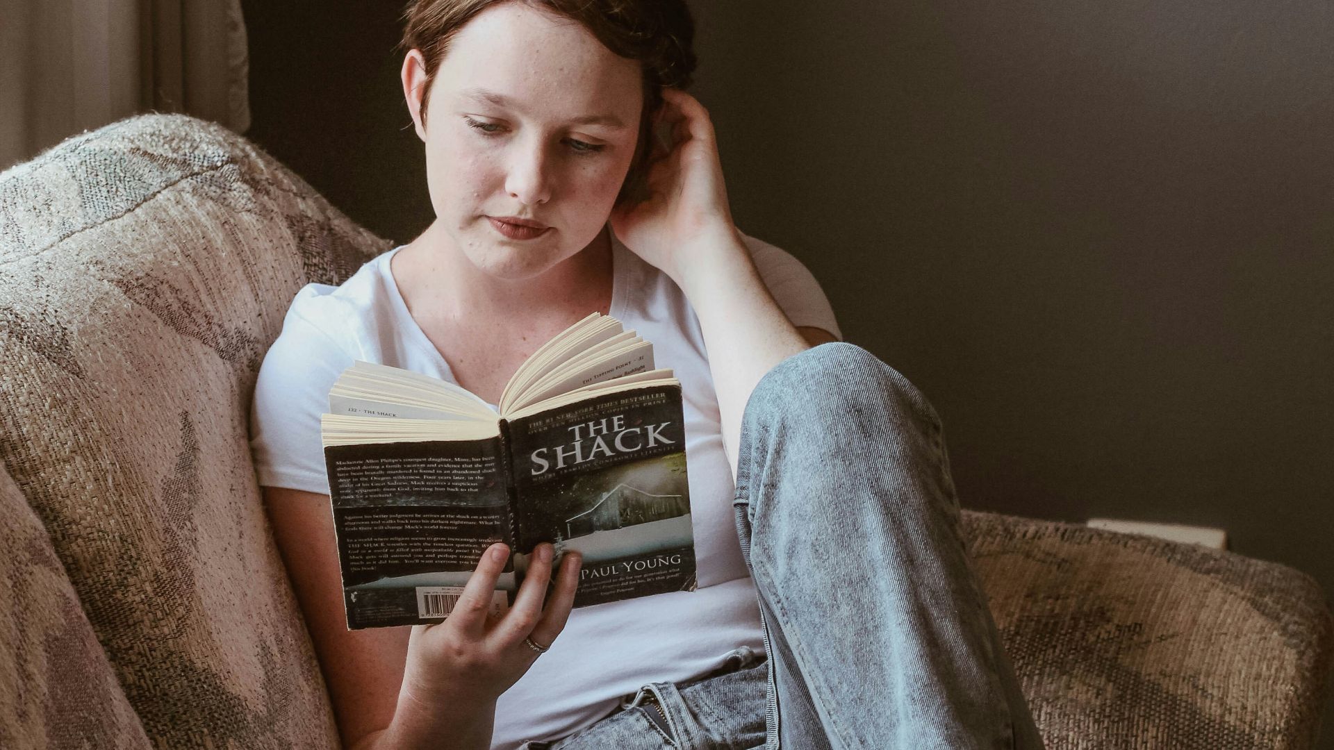 woman sitting on sofa while reading book inside room
