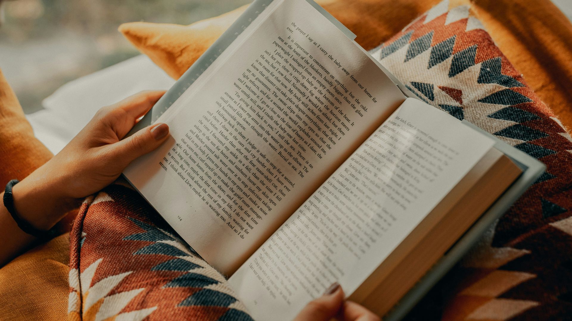 person reading book on brown and beige textile