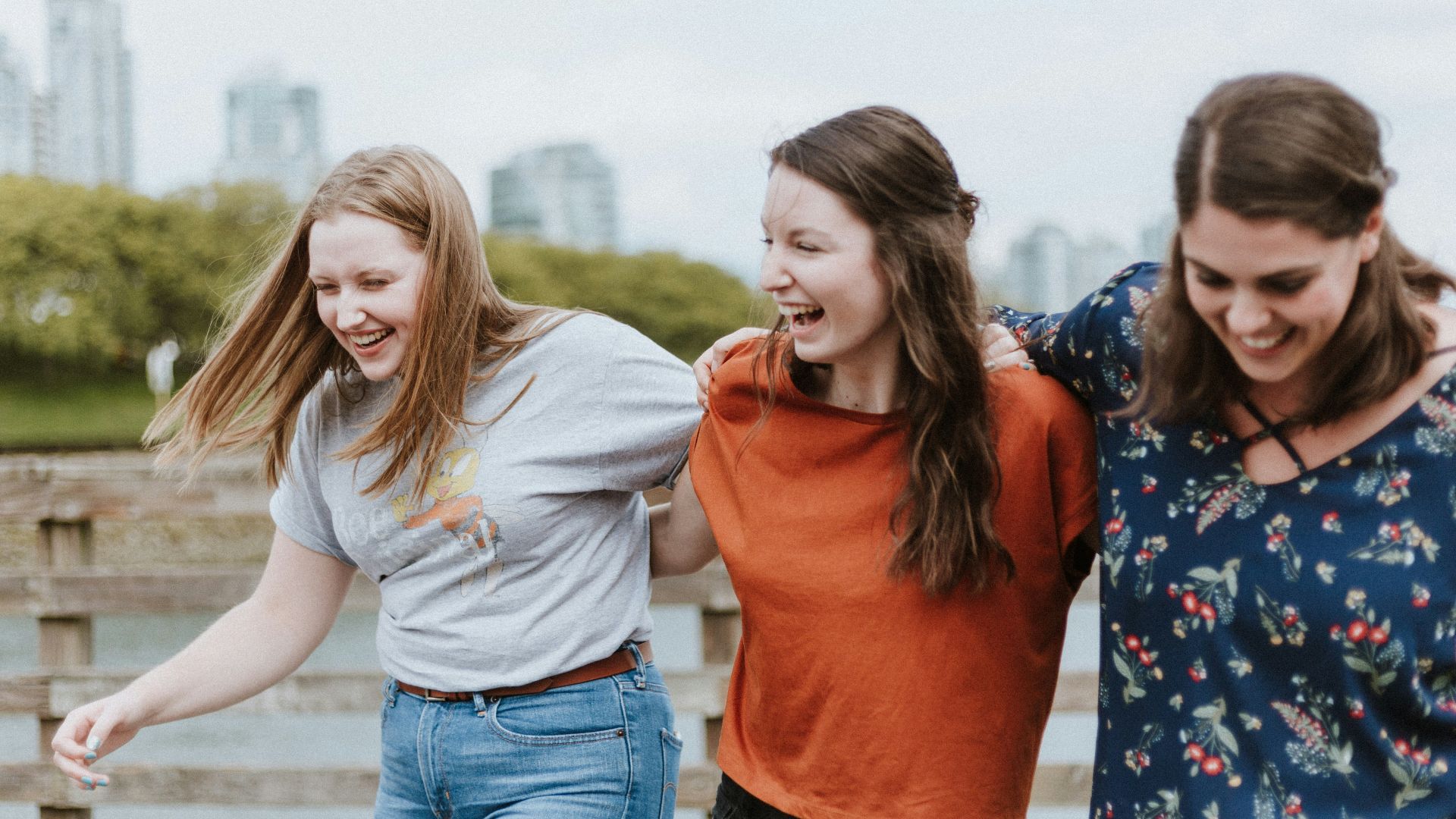 three women walking on brown wooden dock near high rise building during daytime