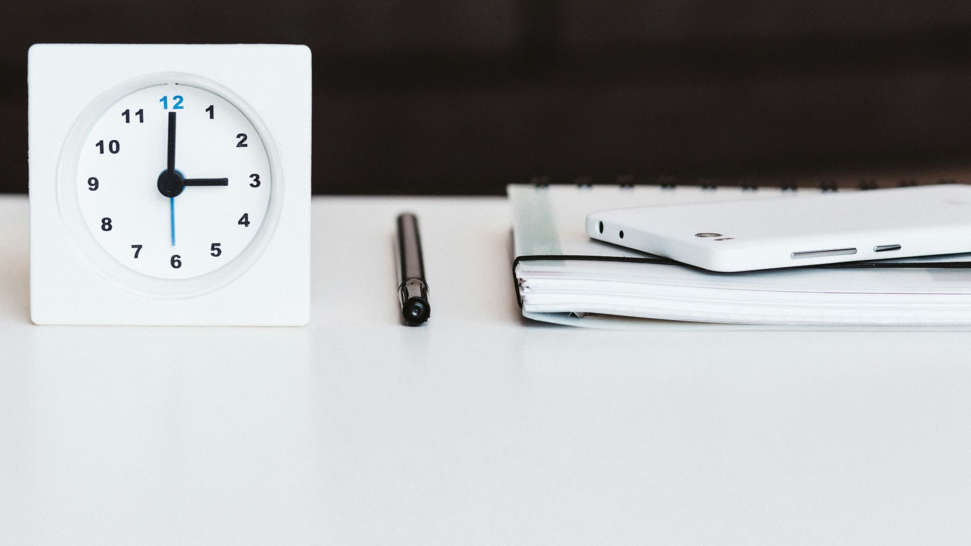 white desk clock near pen and book