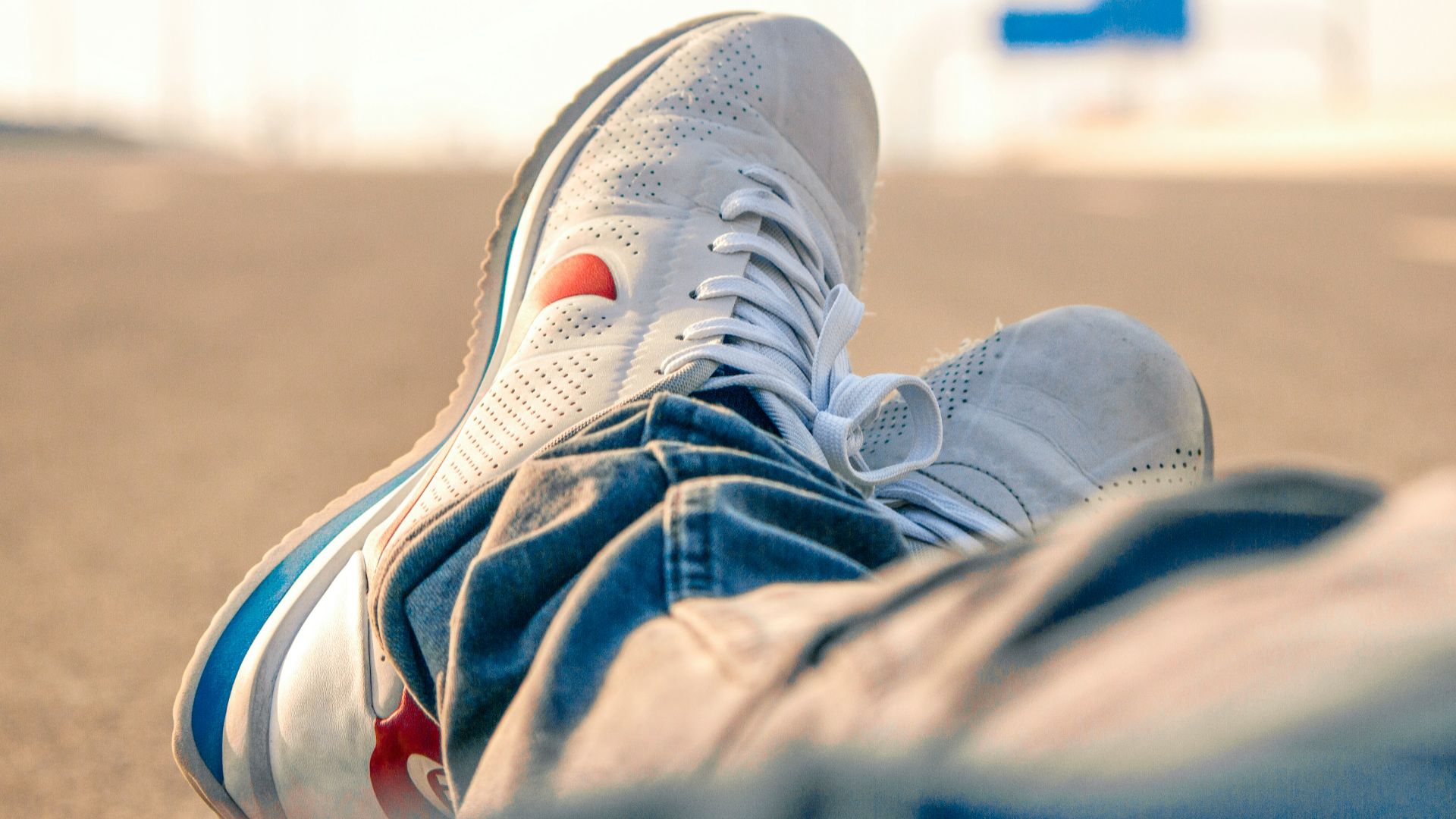 person in white-and-red Nike low-top sneakers and blue denim pants sitting on road during daytime
