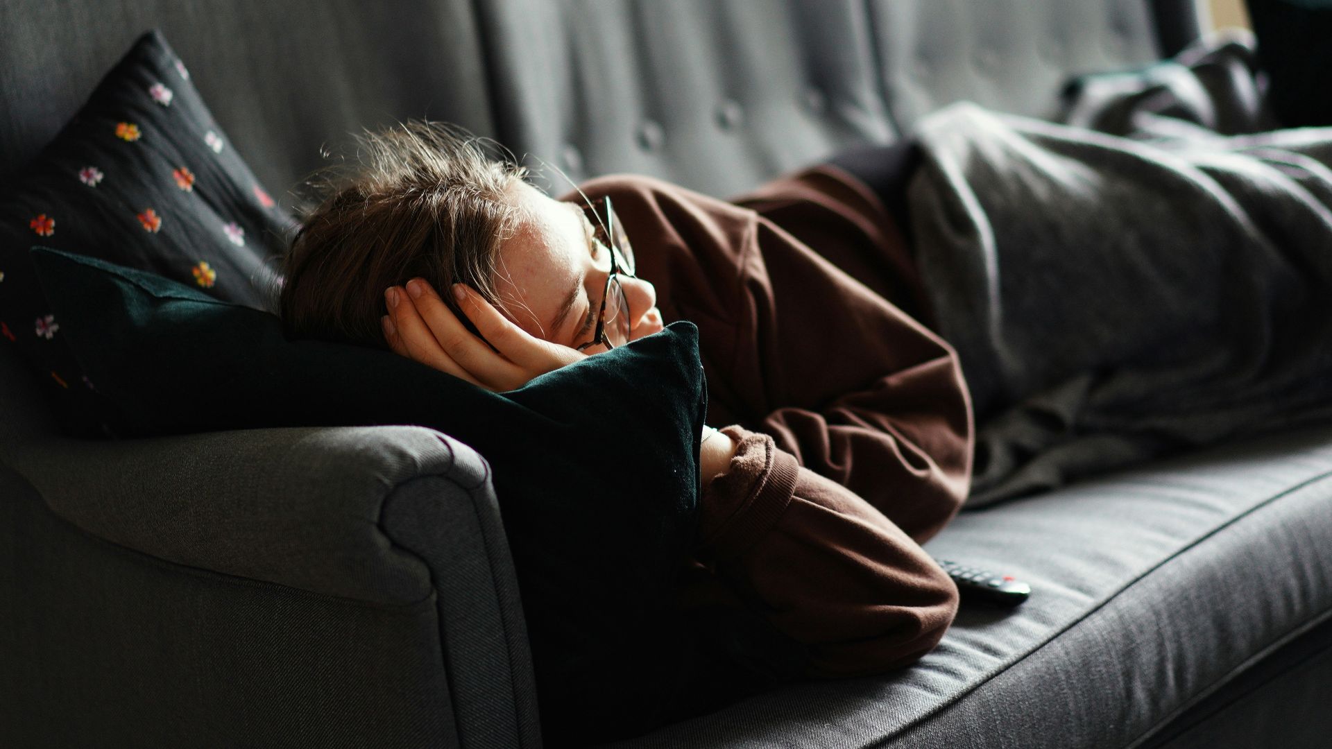 woman in pink jacket lying on gray couch
