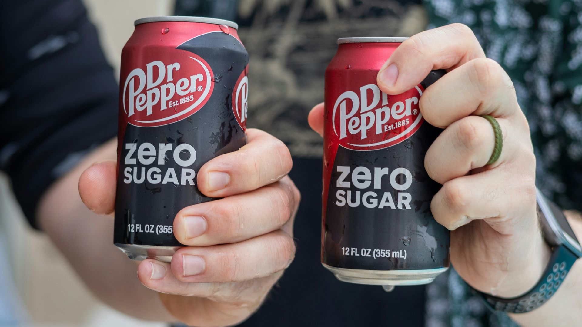 Two people are holding cans of dr. pepper zero sugar.