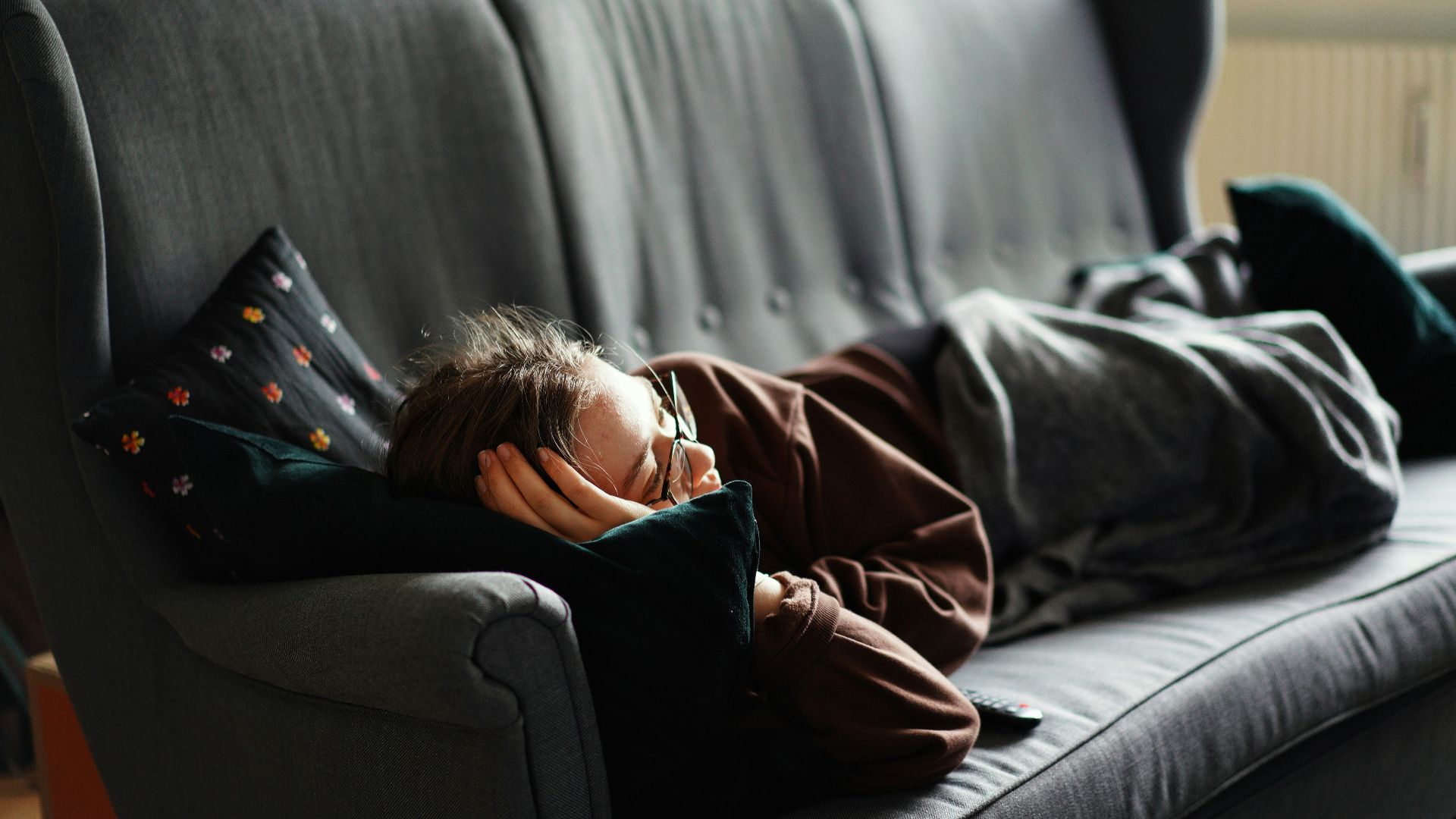 woman in pink jacket lying on gray couch