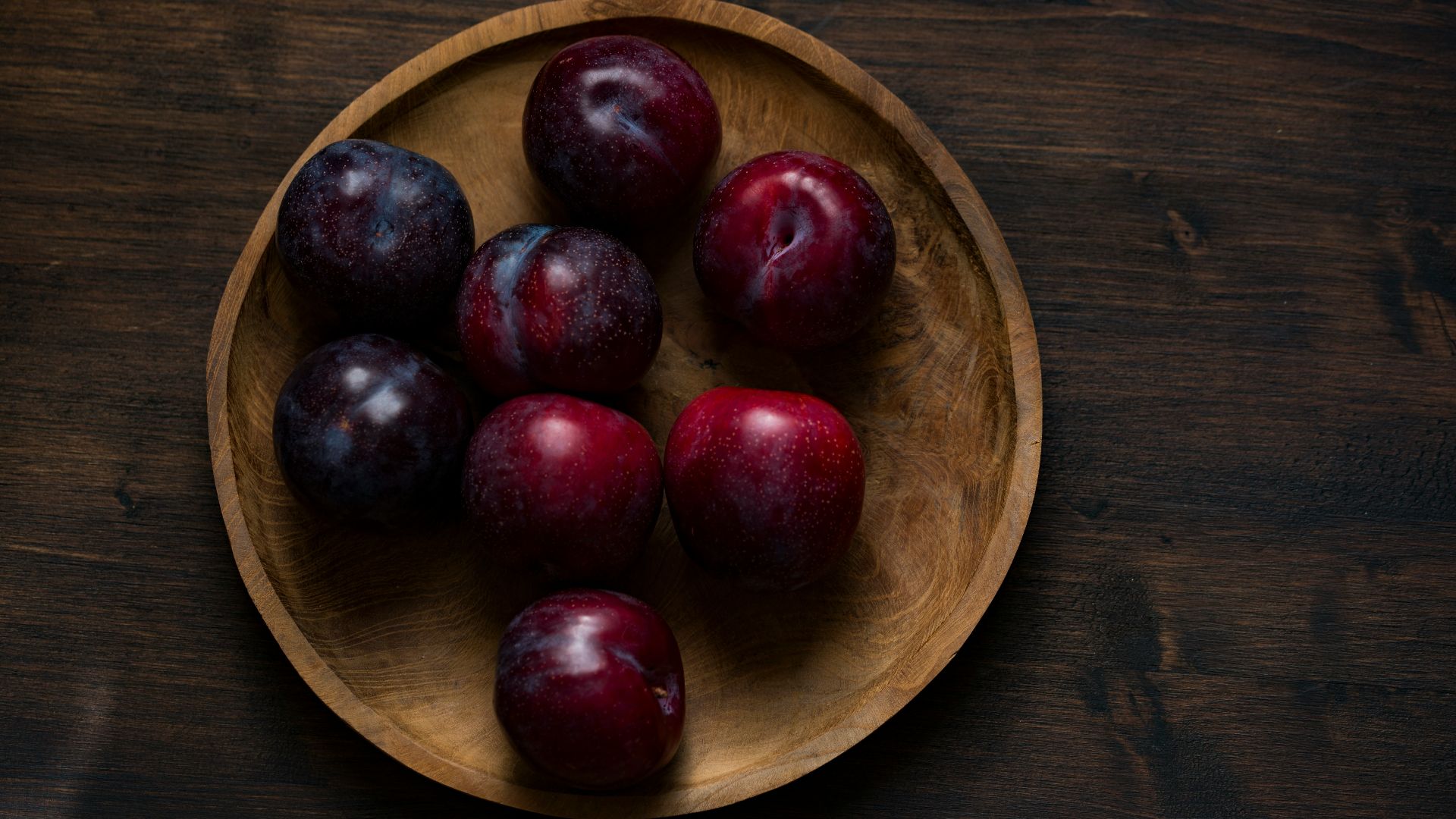red plum fruits on round brown wooden plate