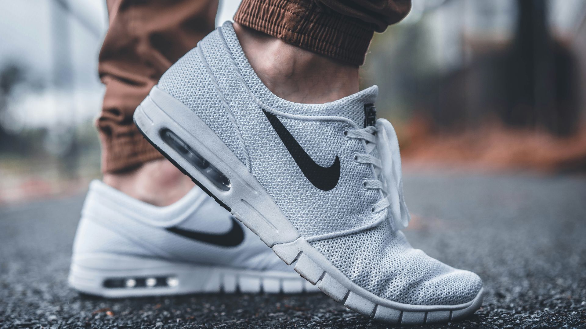 person wearing white Nike running shoes standing on black concrete path