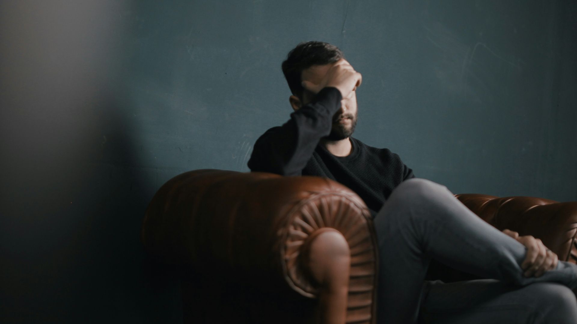 a man holds his head while sitting on a sofa