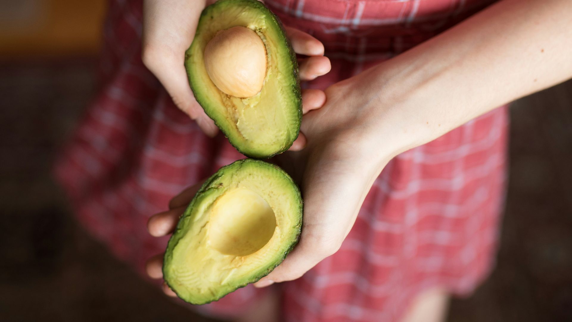 person holding two sliced avocados