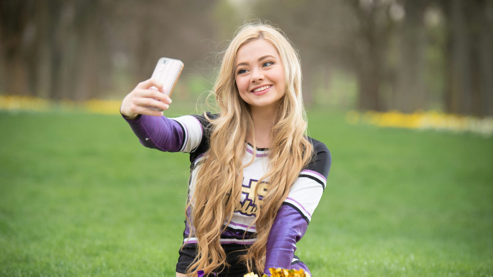 a girl sitting on the grass taking a selfie with her cell phone