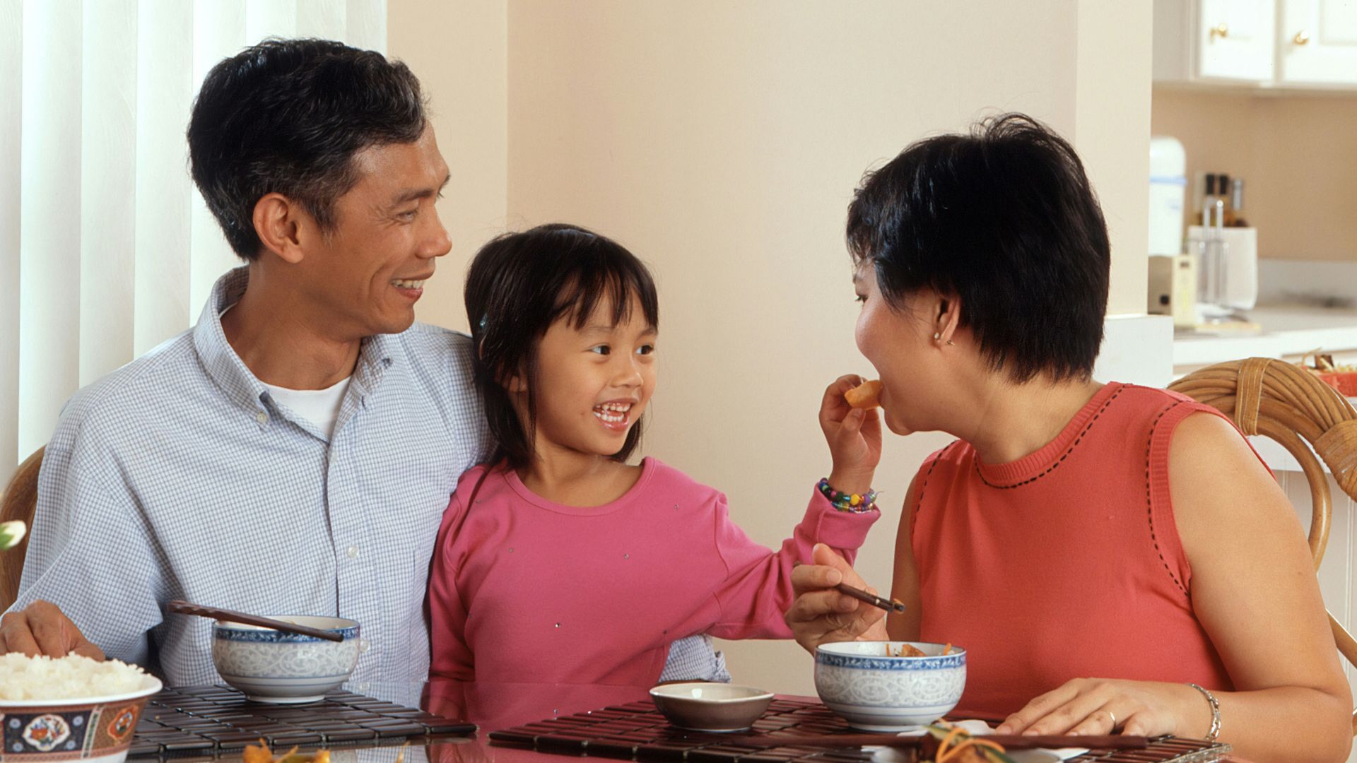 a man, woman and child sitting at a table eating food