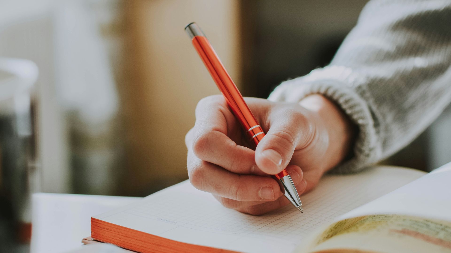 person holding on red pen while writing on book