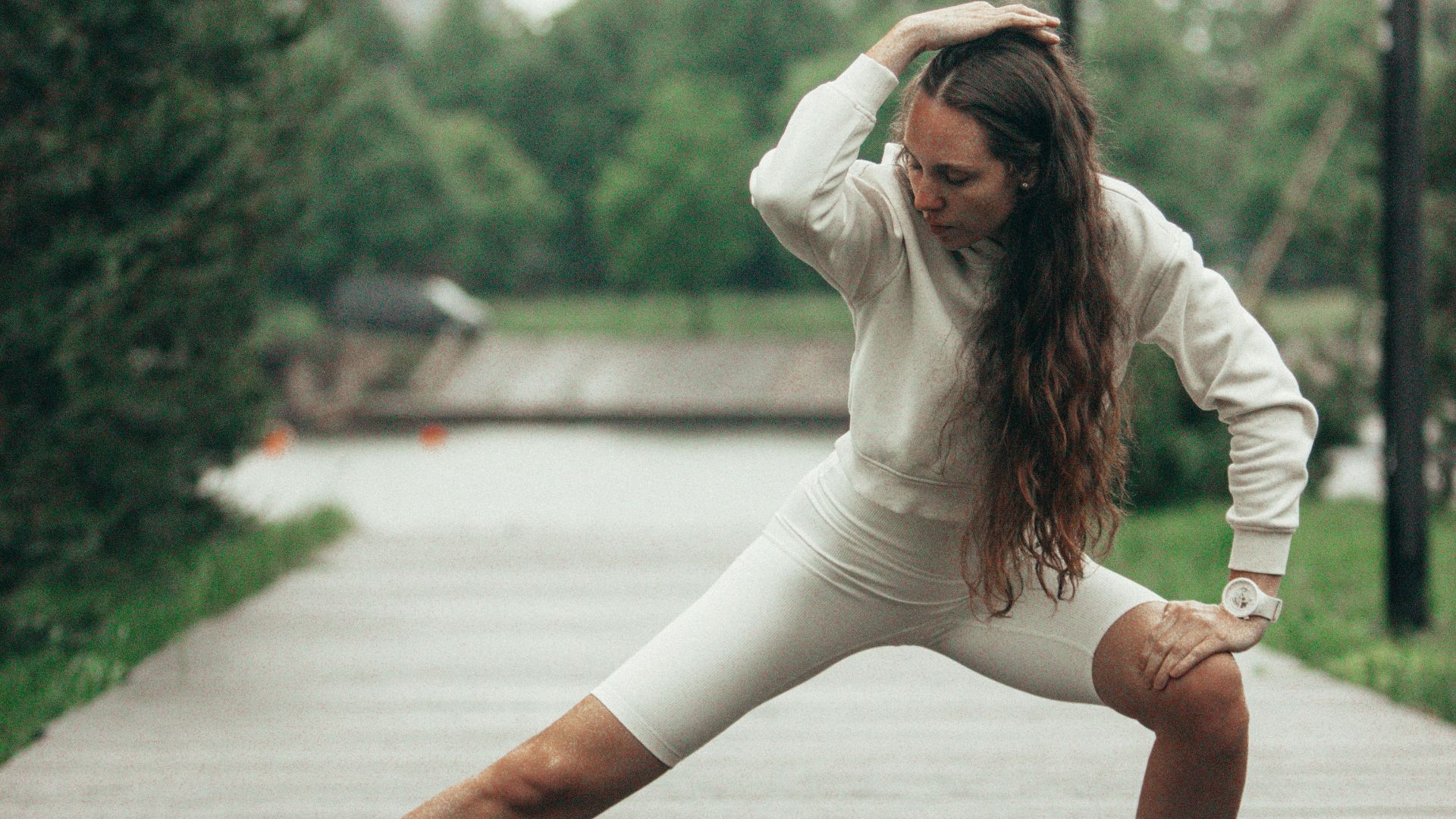 Woman stretches on a wet path after a workout.