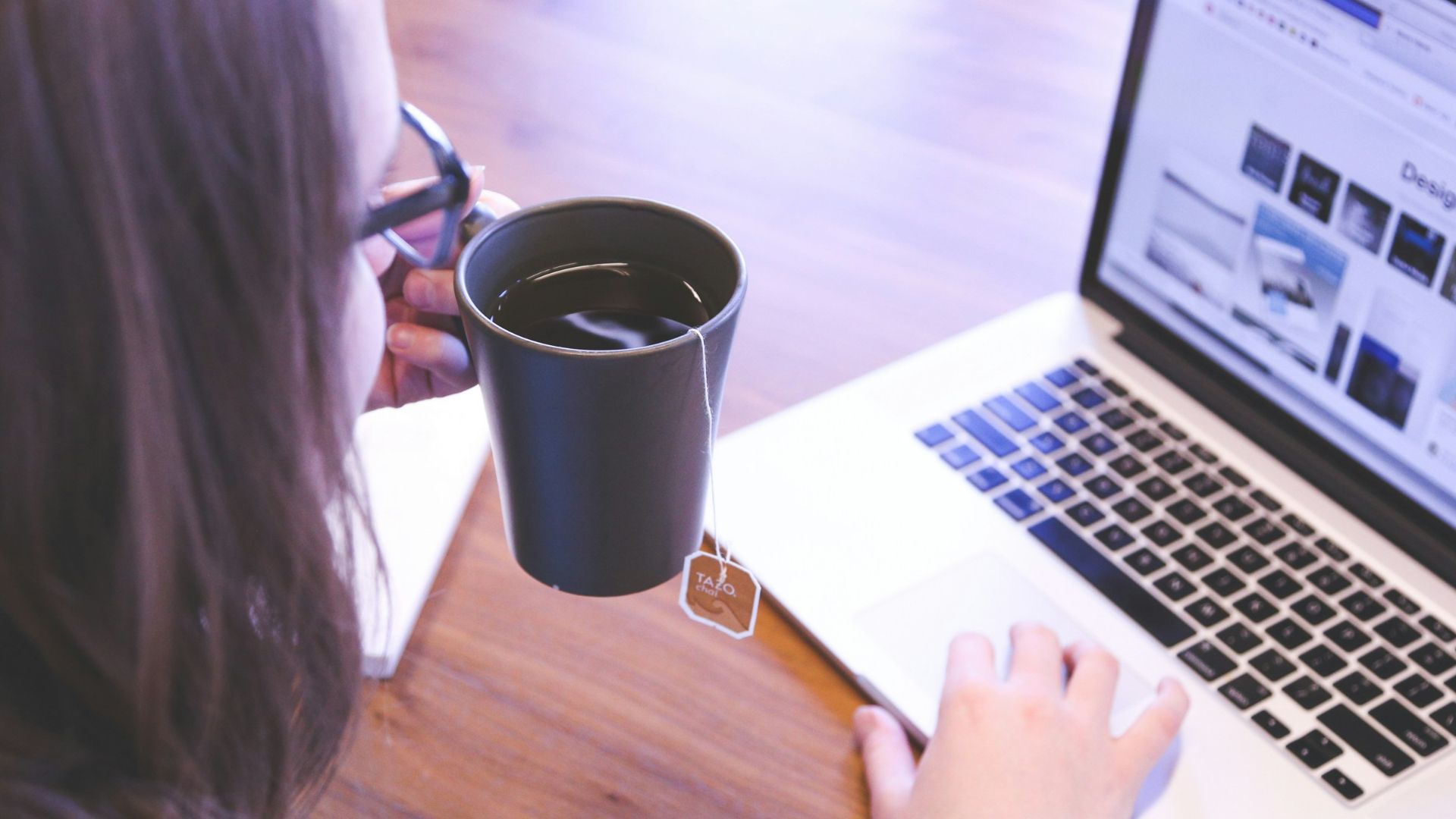 woman holding tea filled mug using MacBook
