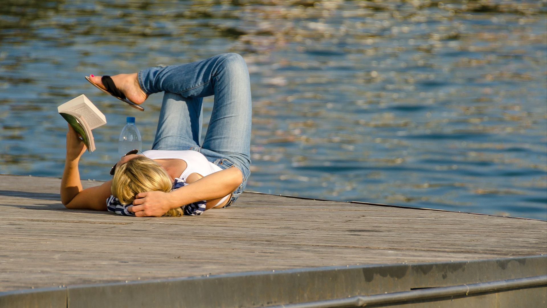 woman in white tank top and gray pants lying on brown wooden dock during daytime