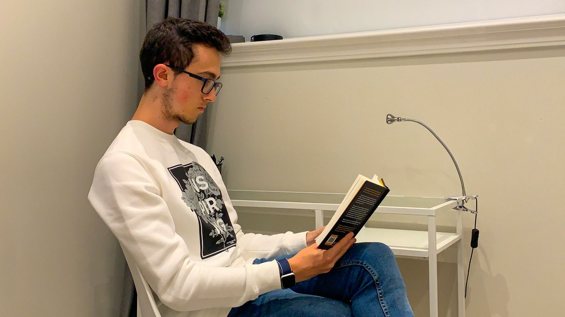 man in white dress shirt and blue denim jeans sitting on white chair reading book