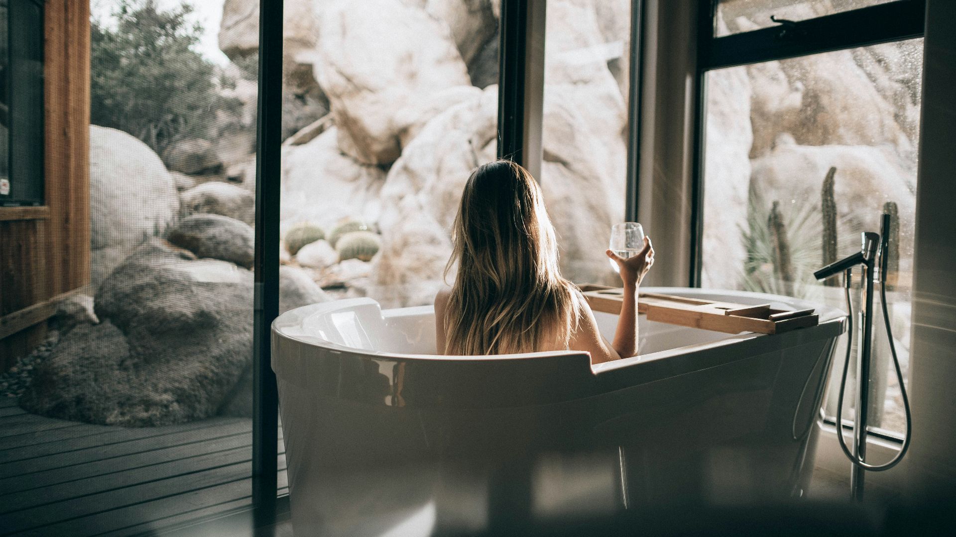 woman in white bathtub holding clear drinking glass
