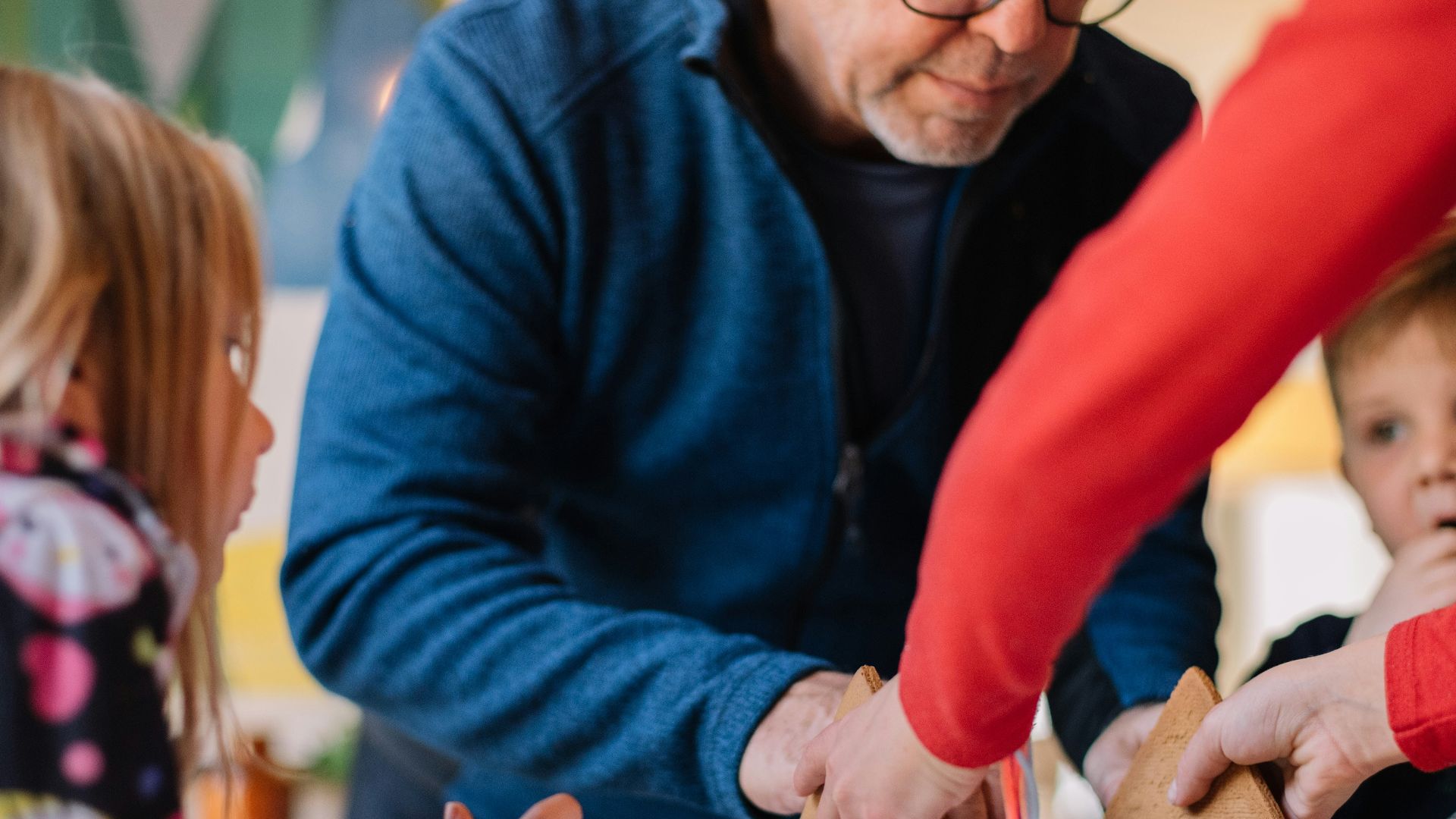 two person making gingerbread house and three children watching them