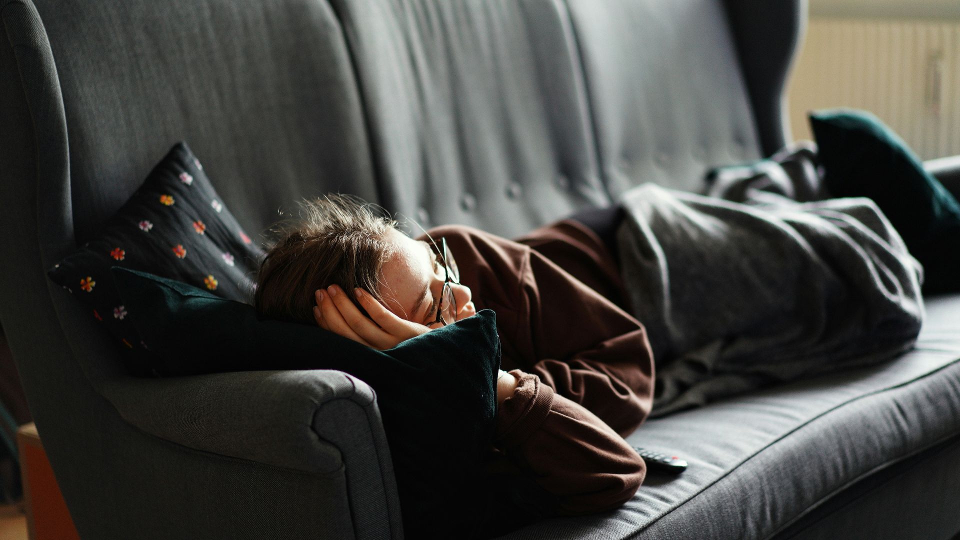 woman in pink jacket lying on gray couch
