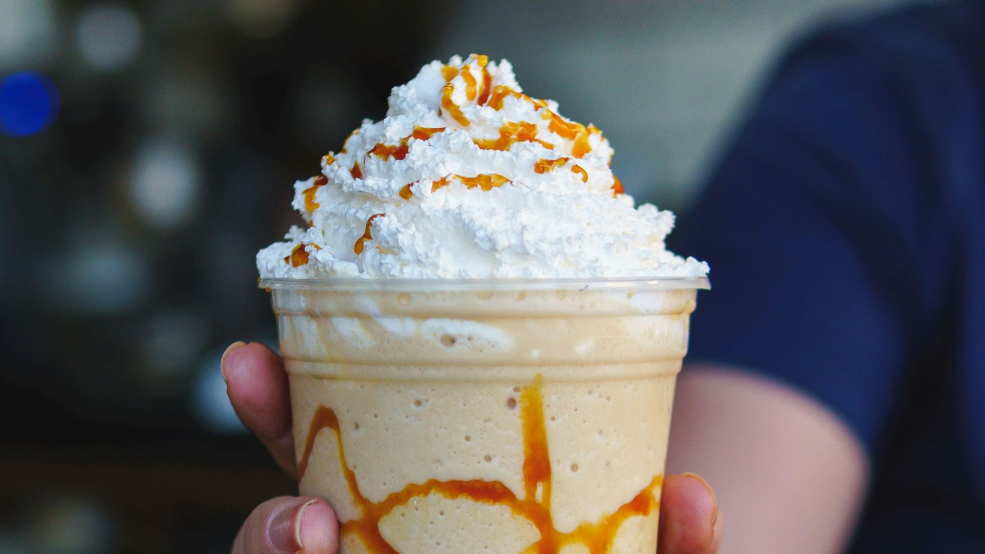 a person holding a cup of ice cream with caramel drizzle