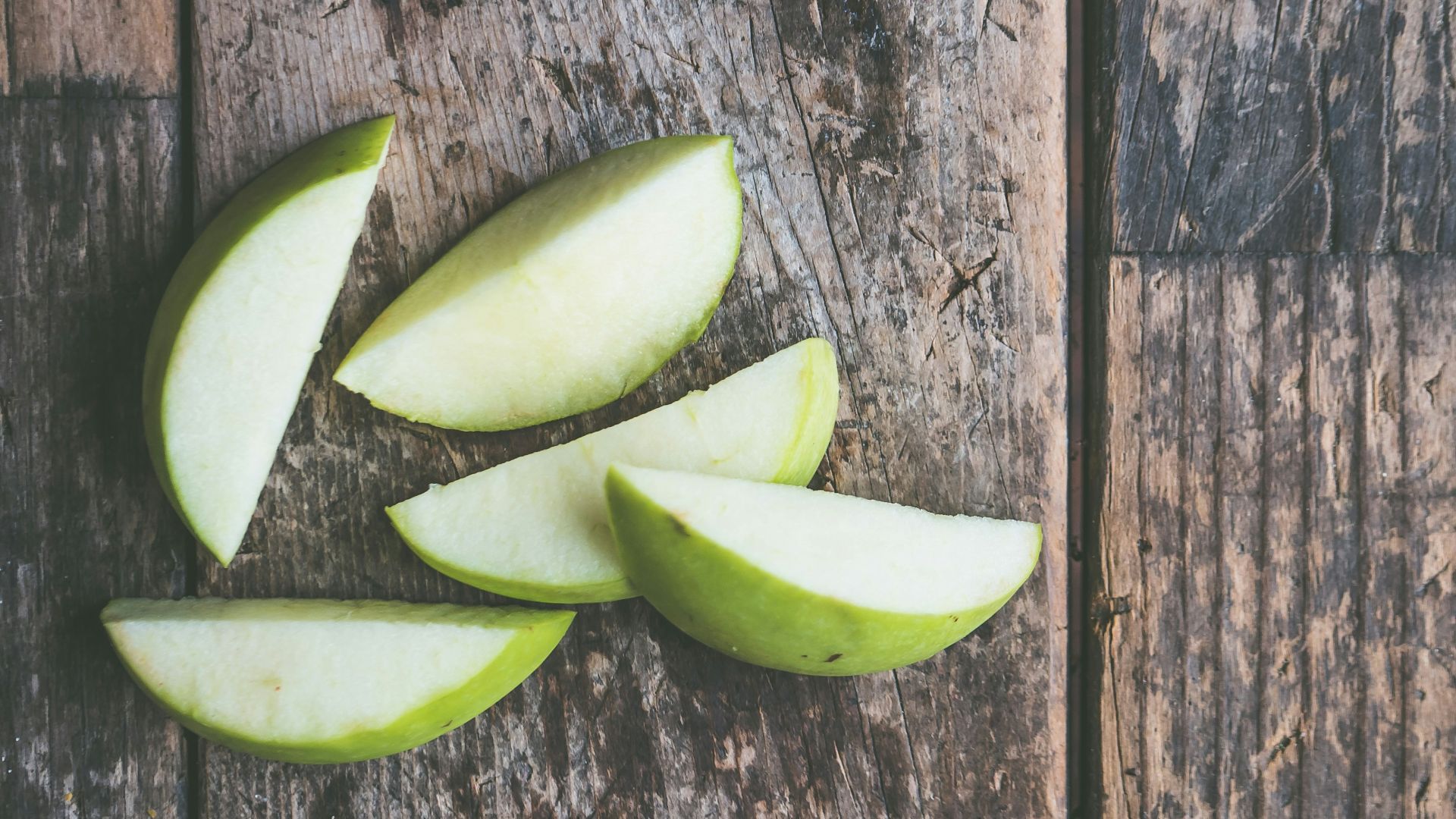five green apple slices on brown wooden panel