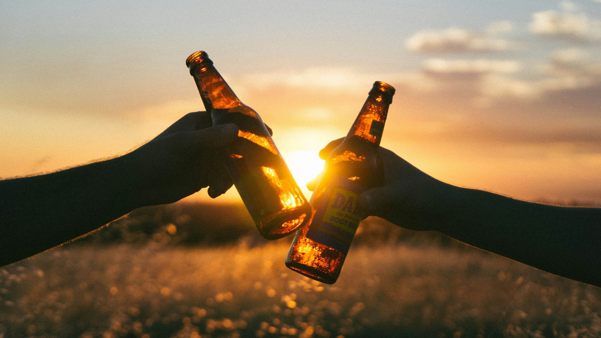 photography of person holding glass bottles during sunset