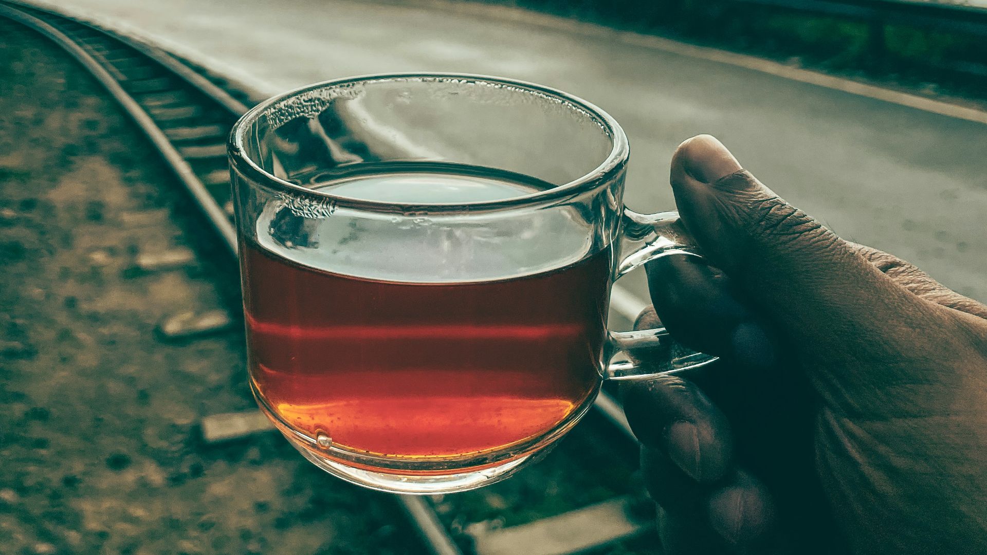 a person holding a glass of tea on a train track