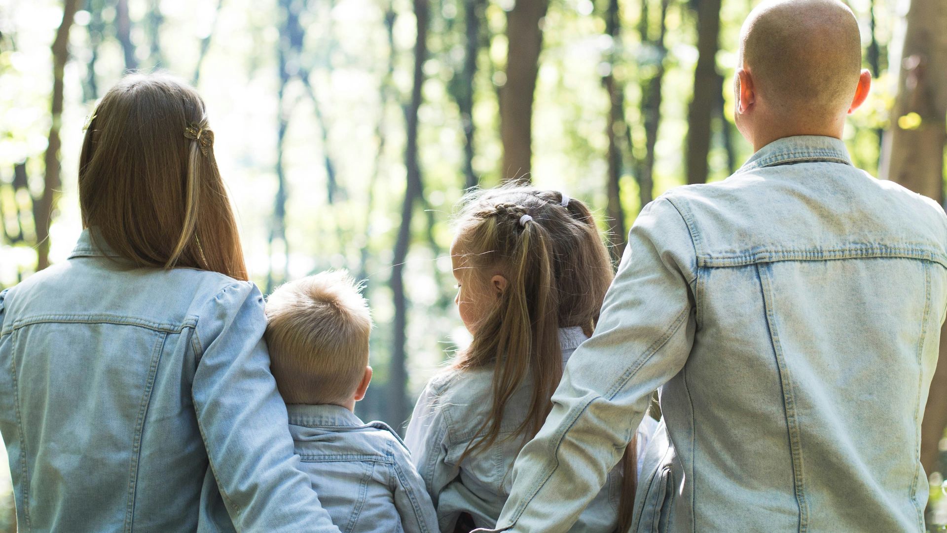 man and woman holding hands together with boy and girl looking at green trees during day