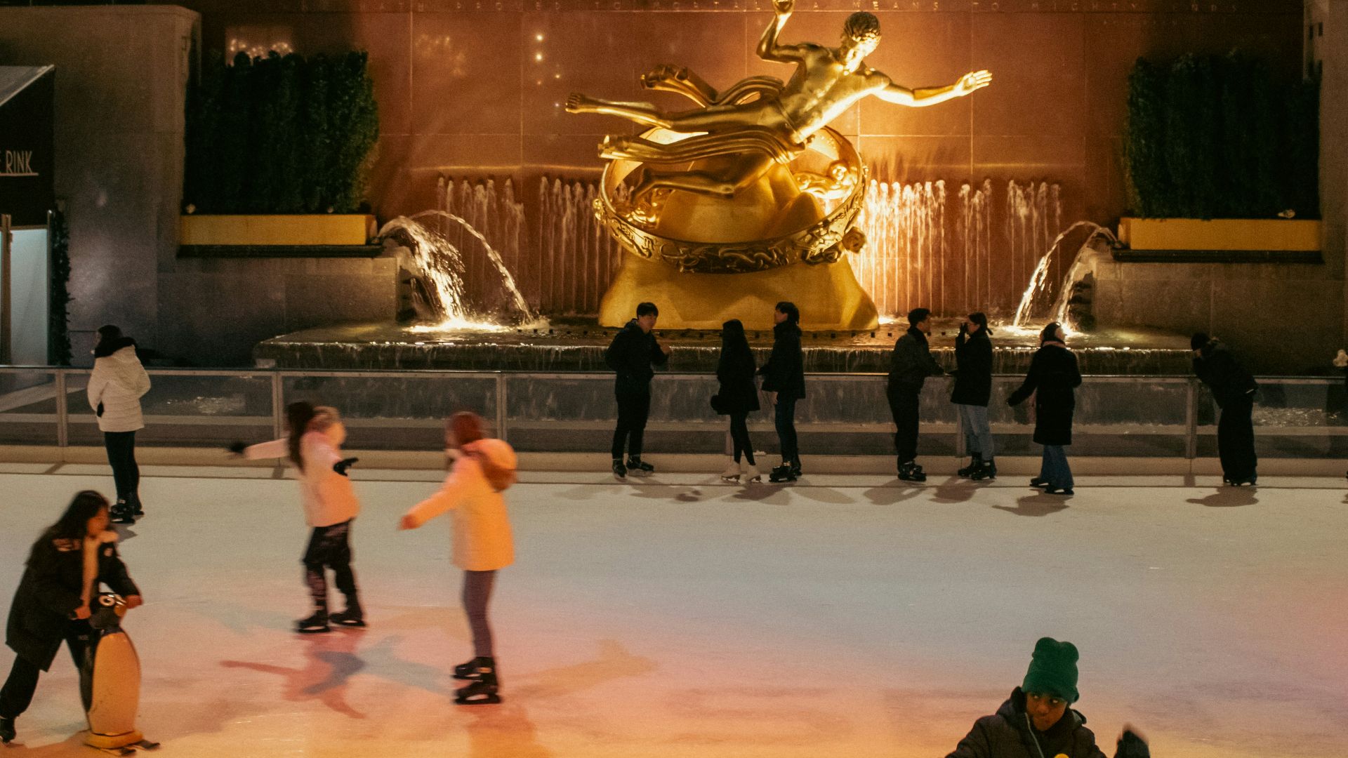 People ice skate in front of a golden fountain.