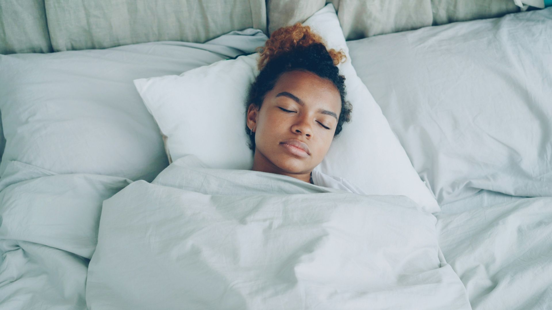 A young woman sleeping peacefully in a white bed.
