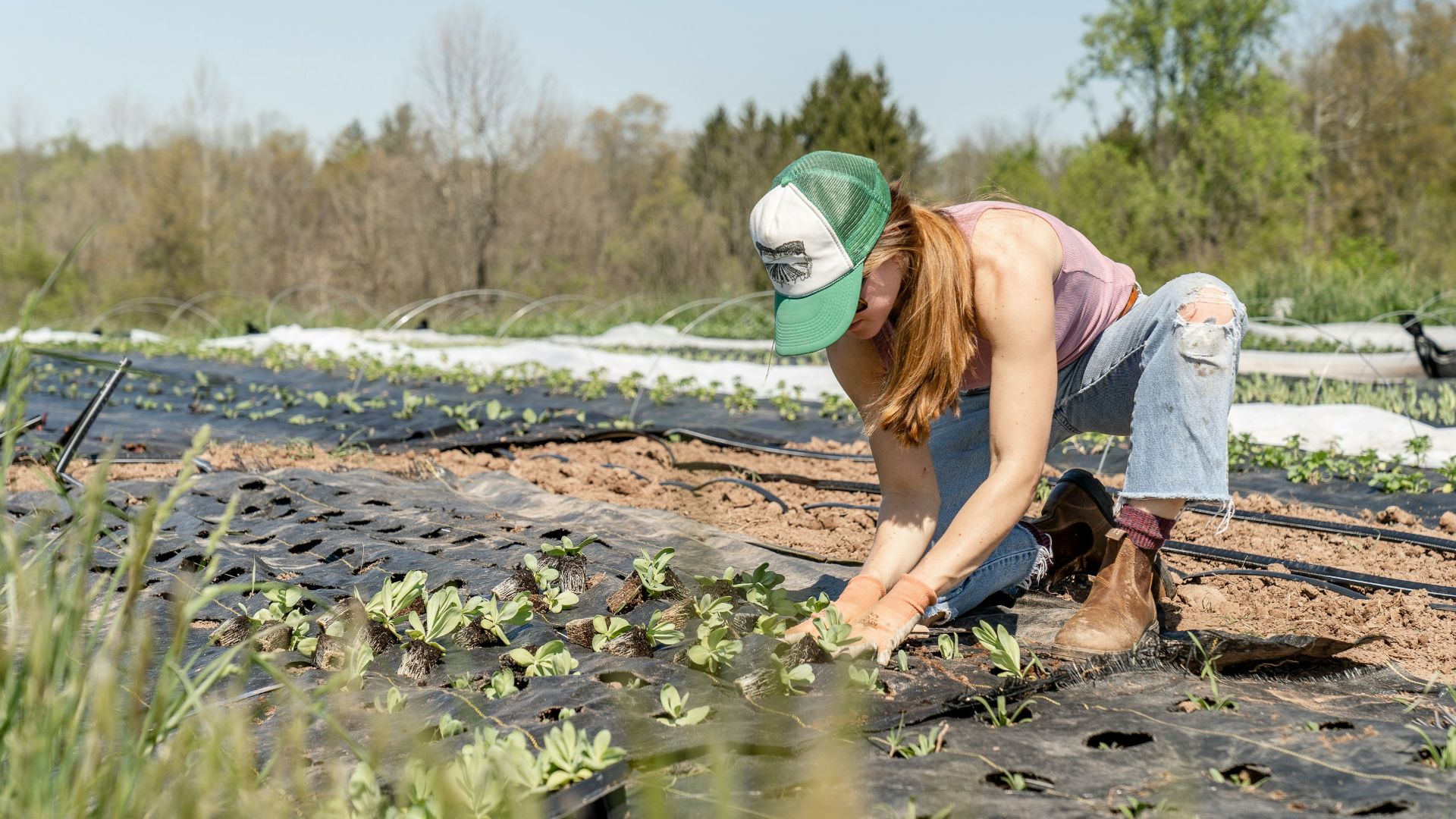 woman in pink shirt and blue denim jeans sitting on brown rock near river during daytime